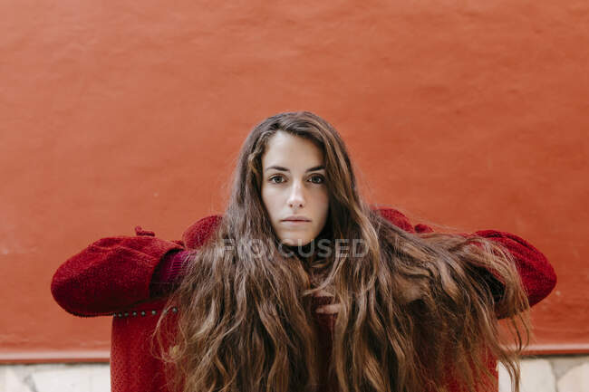 Ritratto di giovane donna sicura di sé con lunghi capelli castani contro la parete rossa — Foto stock