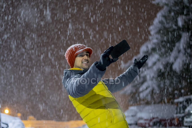 Sonriente hombre tomando una selfie en las nevadas por la noche - foto de stock