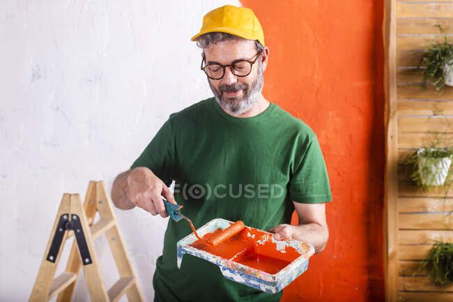 Homem sorridente segurando bandeja de pintura com tinta laranja — Fotografia de Stock