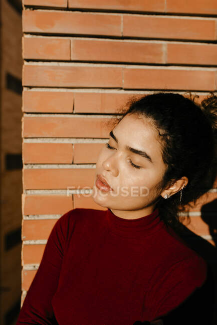Portrait of young woman wearing red turtleneck pullover and enjoying sunlight - foto de stock