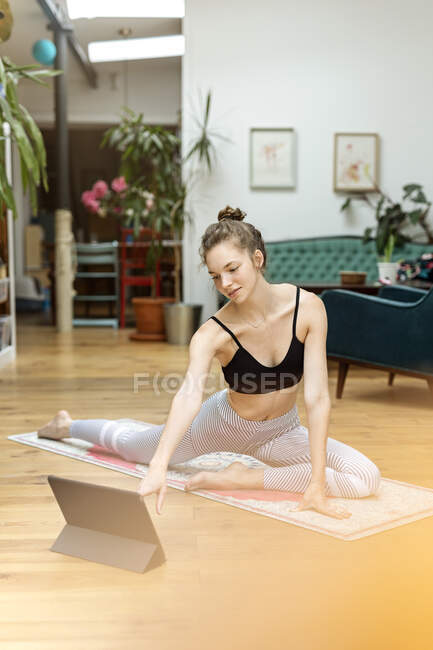 Young woman practicing yoga at home, using yoga app on digital tablet — Stock Photo