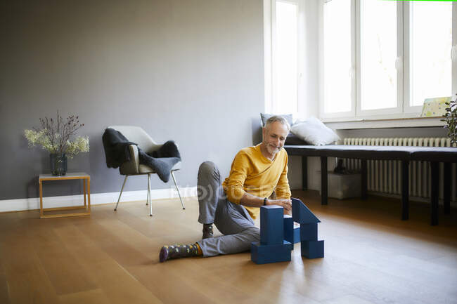 Mature man playing with building blocks on the floor at home — Stock Photo