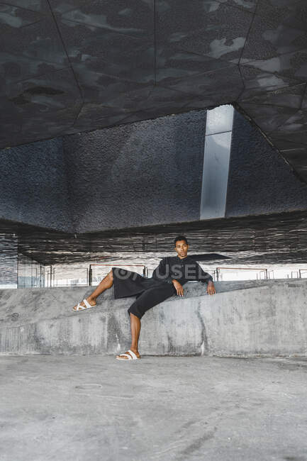 Молодой человек в черном кафтане лежит на бетонной стене под открытым небом — стоковое фото