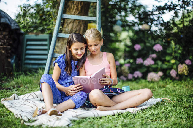 Smiling girls reading a book in garden together — Stock Photo