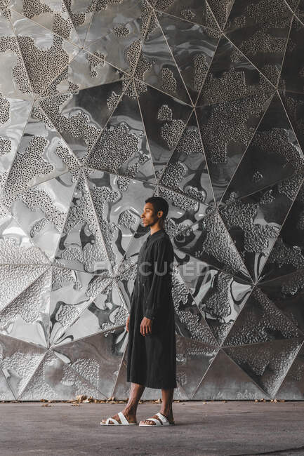 Молодий чоловік у чорному кафті стоїть на структурованій стіні — стокове фото