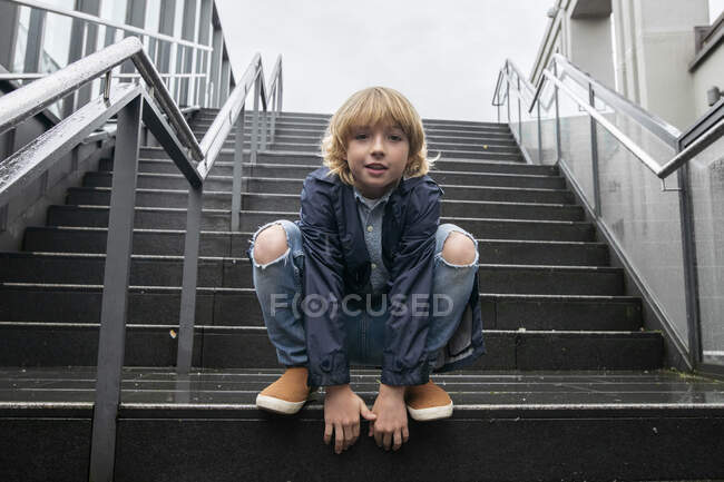 Retrato de menino loiro agachado em escadas ao ar livre — Fotografia de Stock