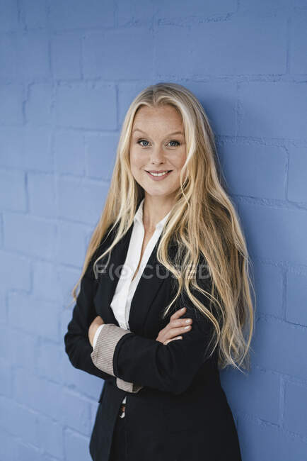 Portrait of a smiling young businesswoman at a blue wall — Stock Photo