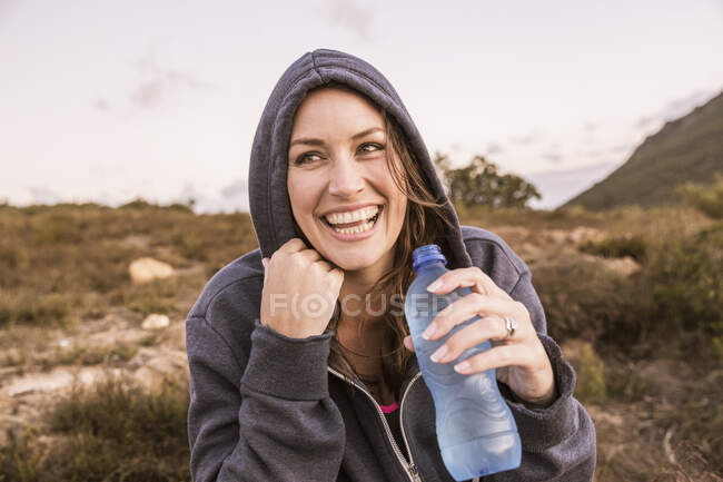 Счастливая женщина с бутылкой воды, отдыхающая от занятий спортом в сельской местности — стоковое фото