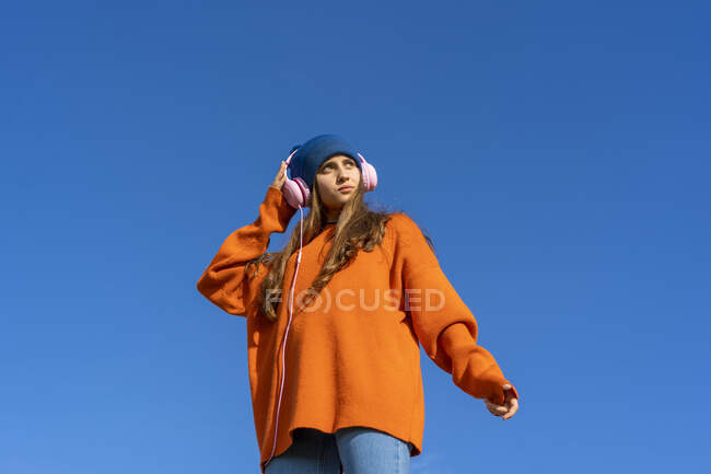 Porträt eines Teenagers vor blauem Himmel, der mit Kopfhörern Musik hört — Stockfoto