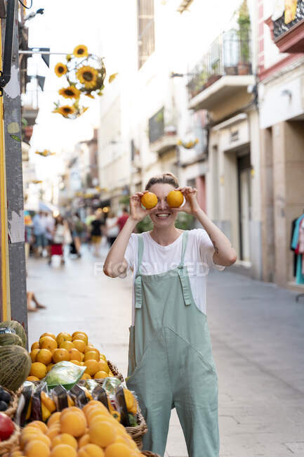 Ridendo giovane donna sulla strada dello shopping che copre gli occhi di arance — Foto stock
