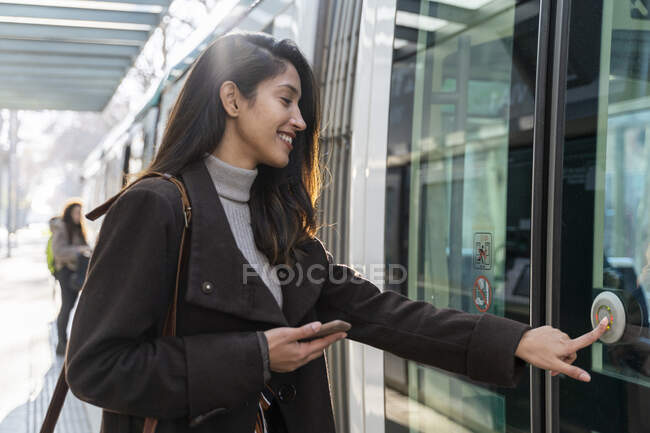Jovencita sonriente presionando el botón en un tranvía - foto de stock