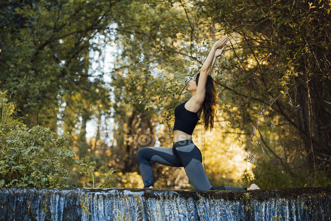 Young woman practicing yoga on a waterfall, bending over back — Stock Photo