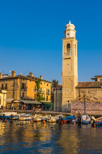 Italia, Provincia di Verona, Lazise, Barche ormeggiate in porto di fronte al campanile della chiesa — Foto stock