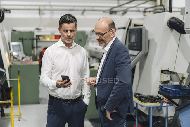 Два бізнесмени, які користуються смартфоном на заводі. — стокове фото