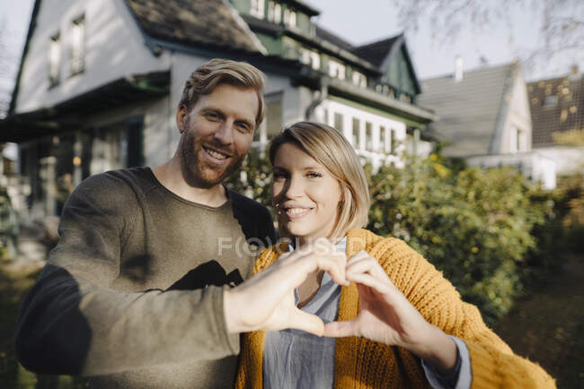 Портрет усміхненої пари, що стоїть перед своїм домом, формує серце руками. — стокове фото
