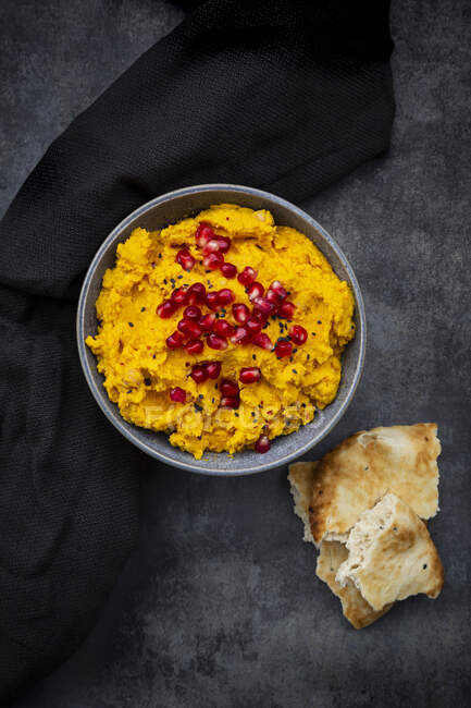 Pita bread and bowl of pumpkin hummus with black sesame and pomegranate seeds — Stock Photo