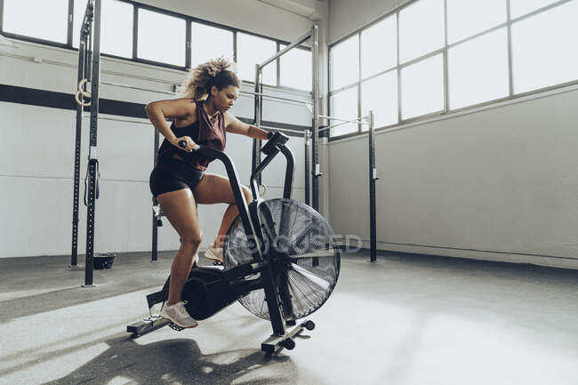 Jeune femme faisant de l'entraînement de vélo pneumatique dans la salle de gym — Photo de stock