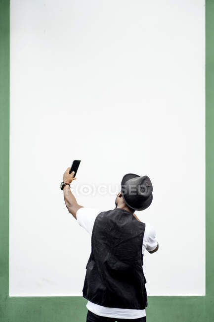 Homme utilisant un smartphone et prenant un selfie devant un mur vert et blanc — Photo de stock