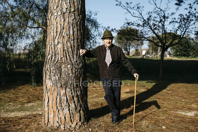 Vecchio con bastone, appoggiato sull'albero nel parco — Foto stock