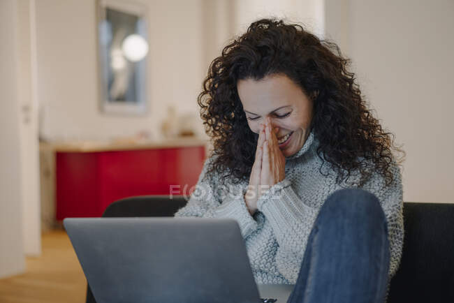 Femme assise à la maison, utilisant un ordinateur portable, riant — Photo de stock
