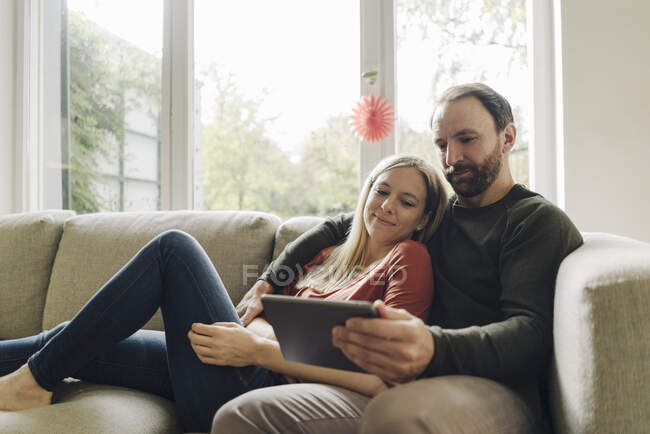 Casal sentado em casa no sofá, usando tablet digital — Fotografia de Stock