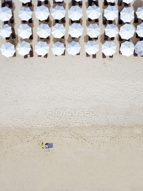 Indonesia, Bali, Vista aérea del hombre tomando el sol frente a filas de sombrillas de playa en la playa costera de arena de Nusa Dua - foto de stock