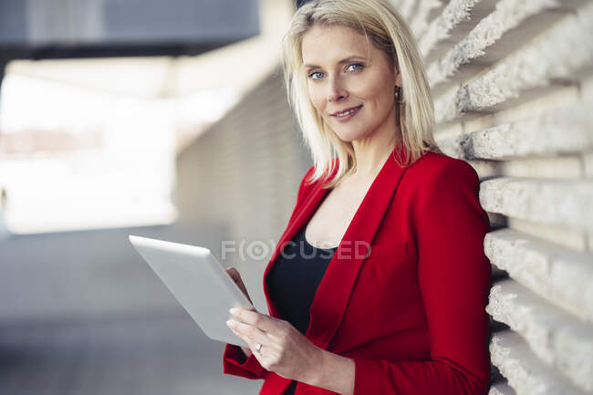 Блондинка бізнес-леді в червоному костюмі і використовує цифровий планшет в офісній будівлі — стокове фото