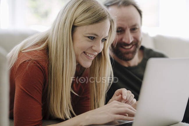 Pareja sentada en casa en el sofá, usando el ordenador portátil - foto de stock