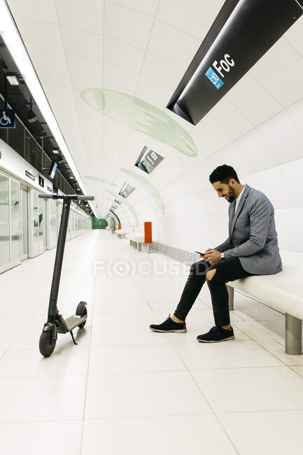 Joven empresario con scooter eléctrico y teléfono celular esperando en estación de metro - foto de stock