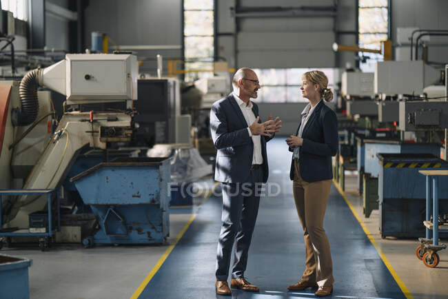Businessman and businesswoman talking in a factory — Stock Photo