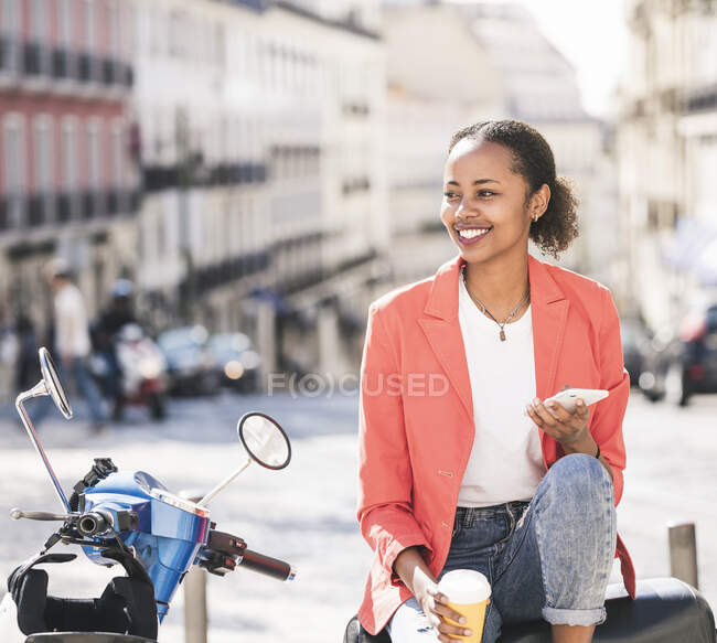 Smiling young woman with motor scooter and cell phone in the city, Lisbon, Portugal — Stock Photo