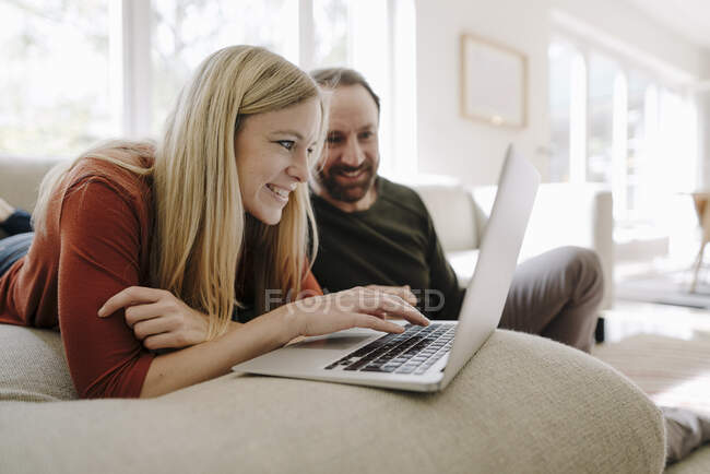 Paar sitzt zu Hause auf Couch und benutzt Laptop — Stockfoto