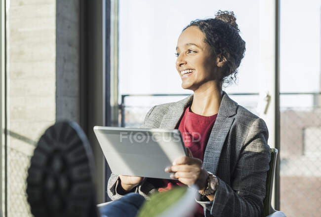 Giovane donna d'affari felice utilizzando un tablet alla finestra in ufficio — Foto stock
