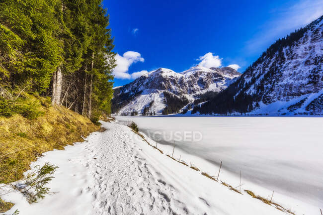 Austria, Tyrol, Tannheim, Snowy footpath stretching along shore of frozen Vilsalpsee lake — Stock Photo