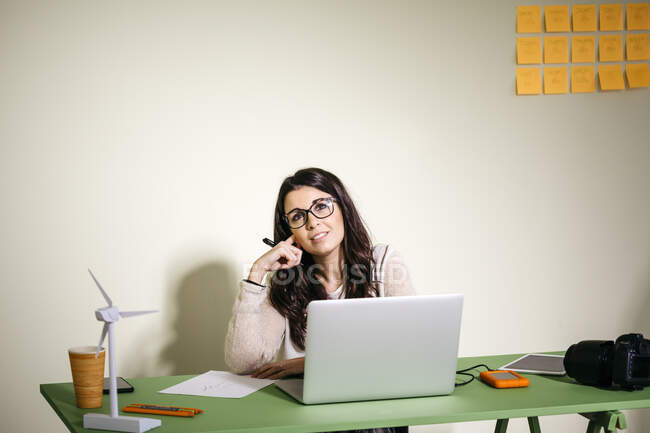 Mujer joven sentada en el escritorio en la oficina pensando - foto de stock