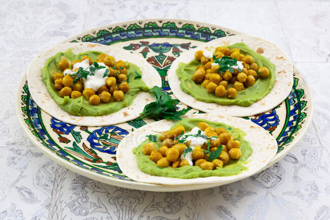 Plate of pita breads with mashed avocados, turmeric chick-peas,yogurtand parsley — Stock Photo
