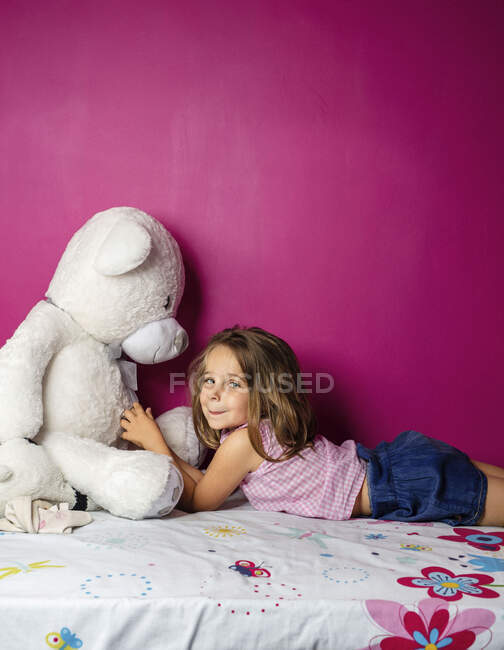 Retrato de niña con gran osito de peluche frente a la pared rosa - foto de stock