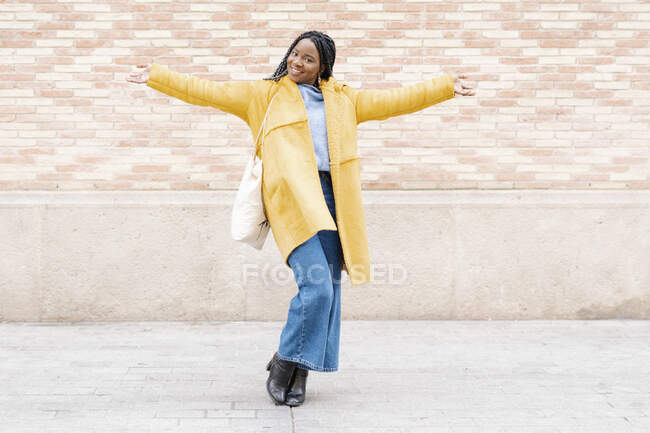 Portrait de jeune femme heureuse portant un manteau jaune debout sur le trottoir — Photo de stock