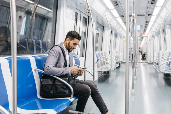 Young businessman with cell phone and earphones on the subway — Stock Photo