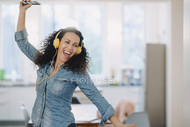 Счастливая женщина слушает музыку, поет и танцует, используя смартфон и наушники — стоковое фото