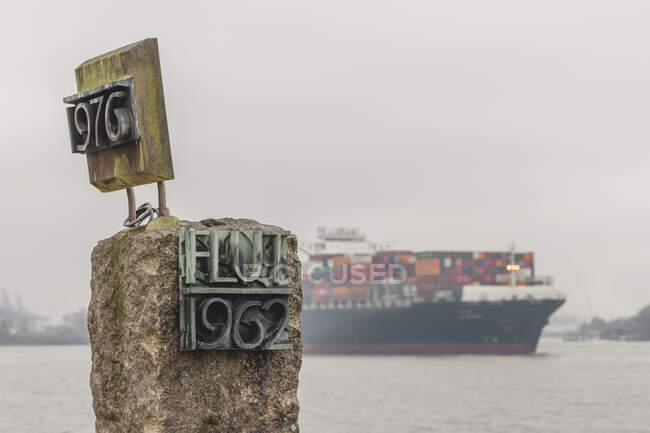 Germany, Hamburg, Coastal flood memorialwith container ship in background — Stock Photo