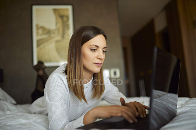 Businesswoman lying on bed in hotel room using laptop — Stock Photo