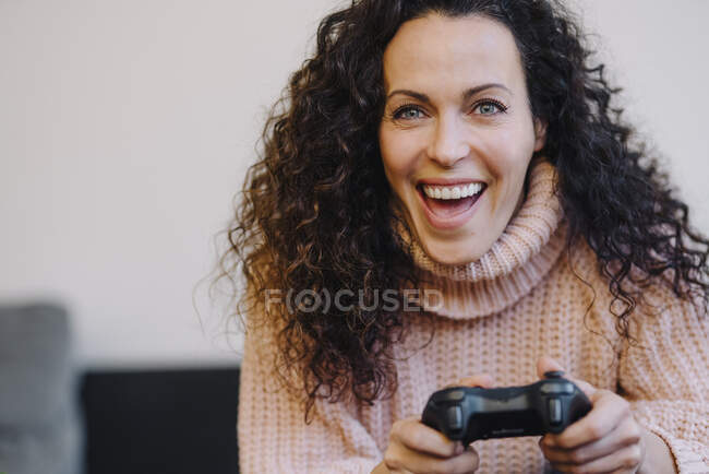 Femme assise sur le canapé, s'amusant, jouant avec une console de jeu, portrait — Photo de stock
