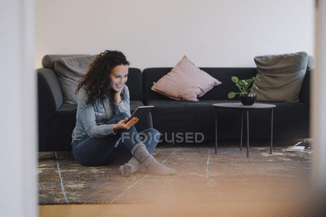 Жінка сидить вдома на підлозі, користуючись цифровим планшетом, читає — стокове фото