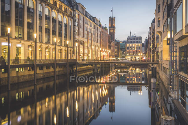 Deutschland, Hamburg, Straßenlaternen beleuchten Gebäude entlang des glänzenden Elbkanals in der Abenddämmerung — Stockfoto