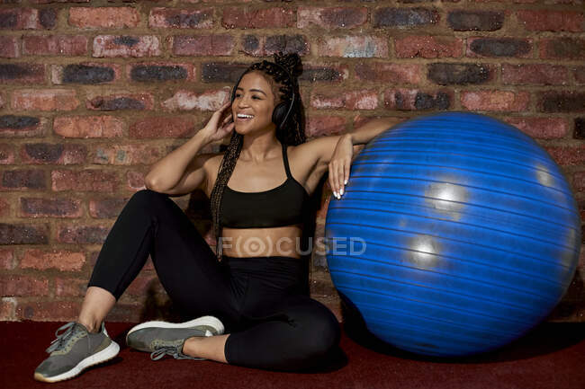 Atleta donna con pallone da ginnastica, seduta sul pavimento, che ascolta musica — Foto stock