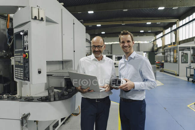 Portrait of two smiling men in a factory with laptop and VR glasses — Stock Photo
