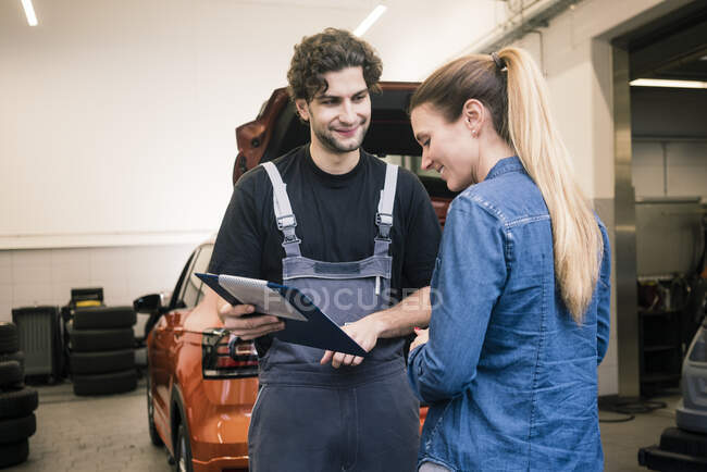 Mecánico de coches mostrando lista ckeck al cliente en el taller - foto de stock