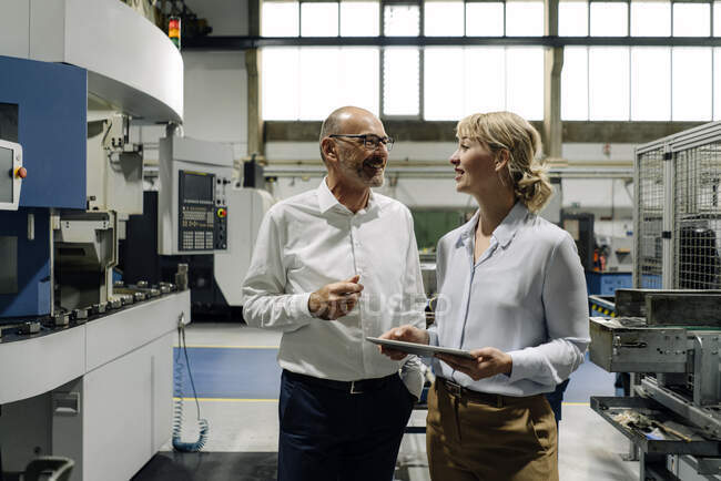 Man and woman with tablet talking in a factory — Stock Photo