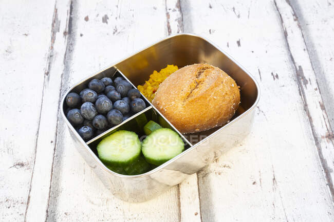 Lunch box with cucumber slices, blueberries and bun with lentil paste — Stock Photo
